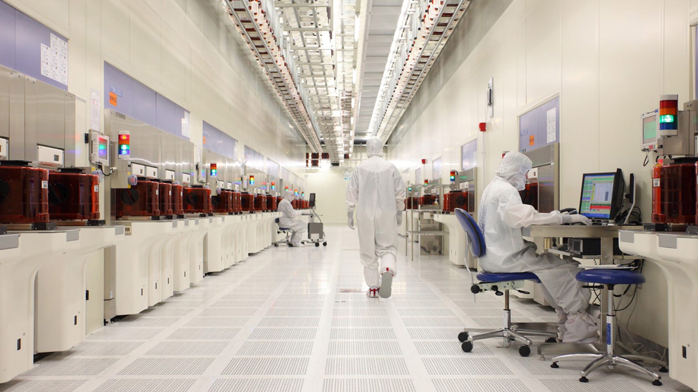 two lab workers in full body ppe suits sitting while another walks through lab