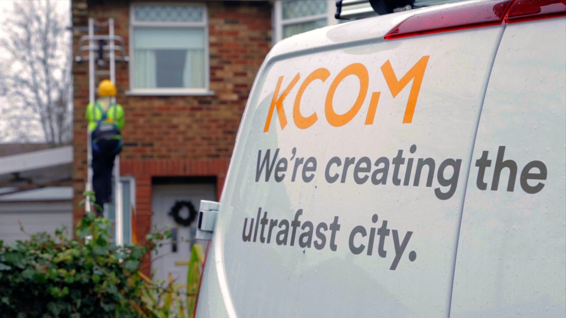kcom van with worker in hi-vis climbing a ladder on wall of a home in background
