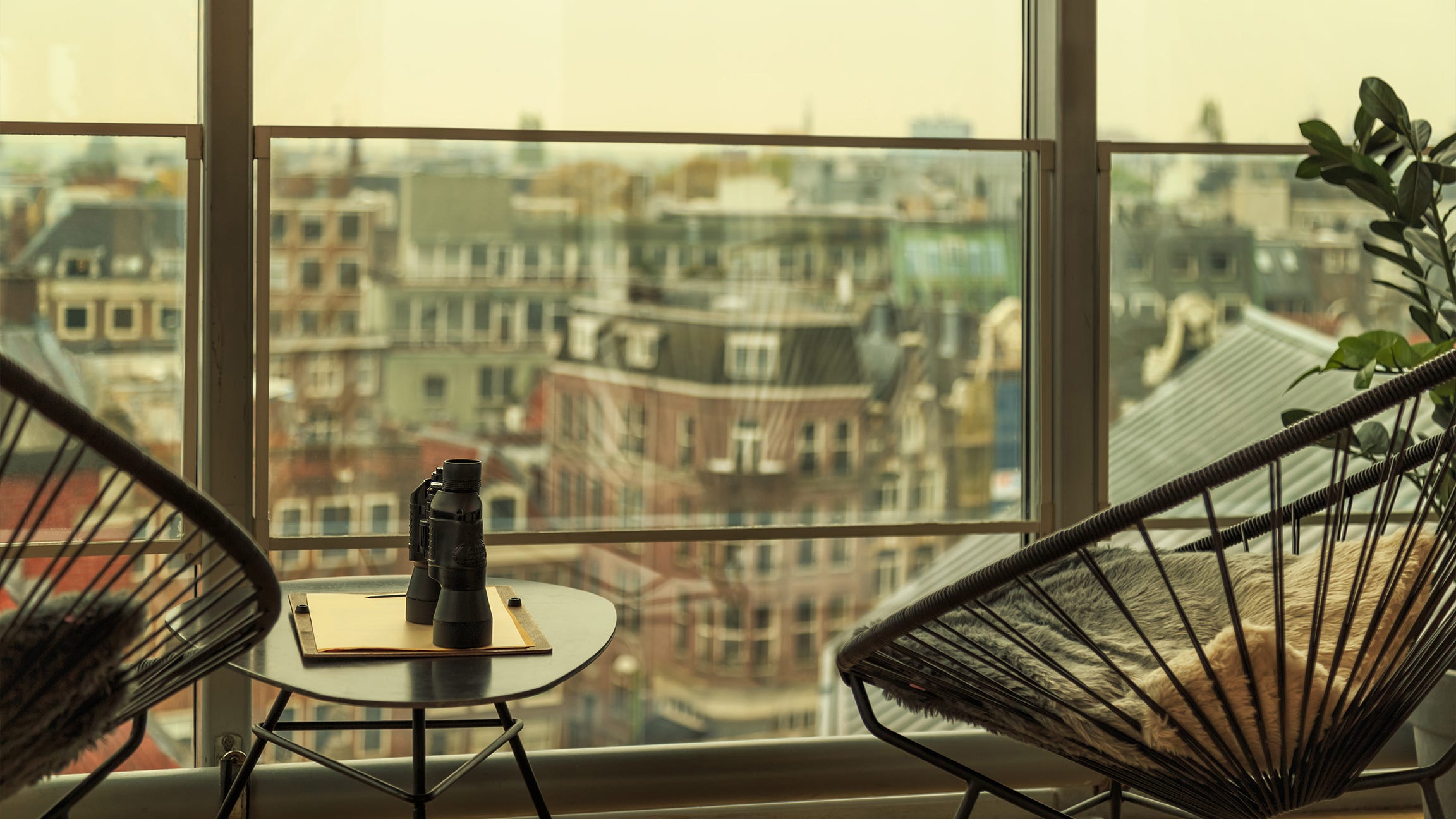 two chairs with table in between holding binoculars and notepad, facing out at buildings