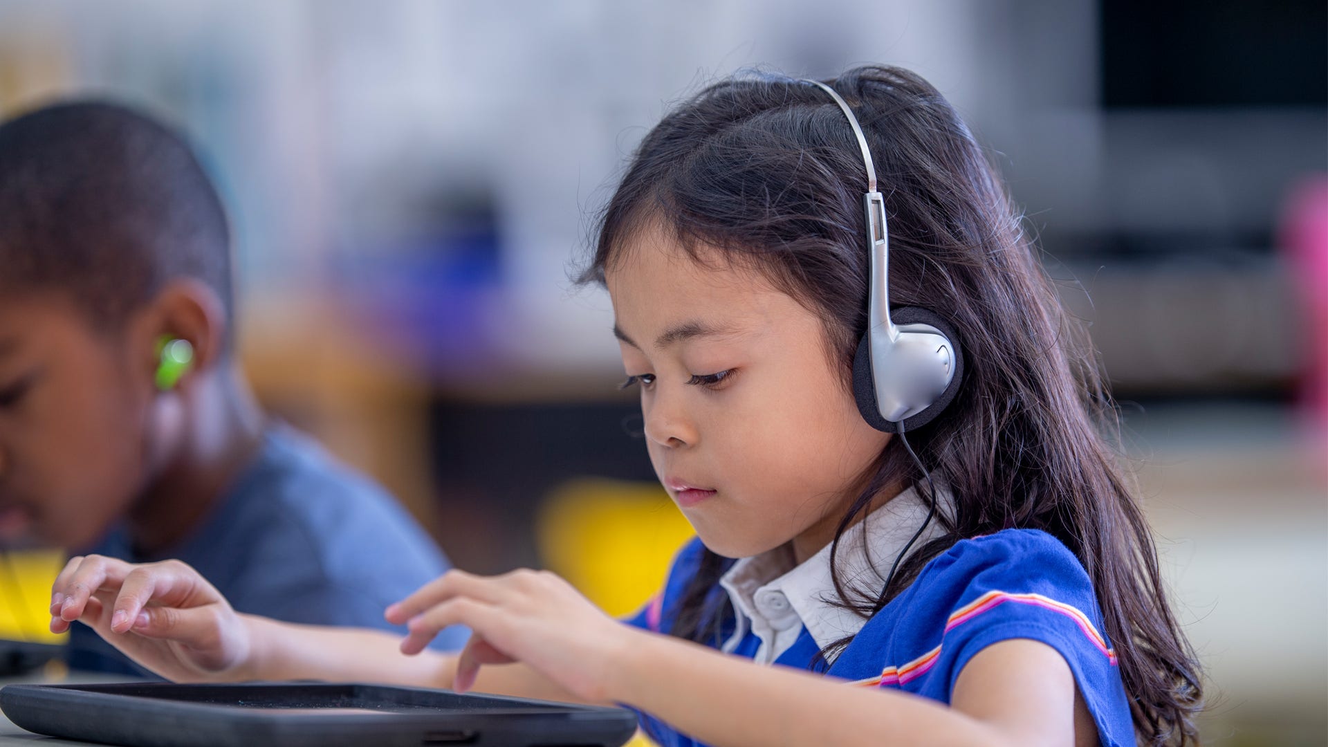 child sitting at desk with headphones on and using a tablet