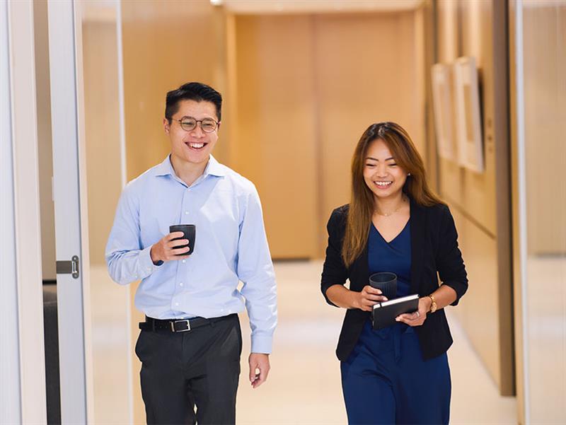 Male and female workers smiling and walking down a hallway in an office setting.