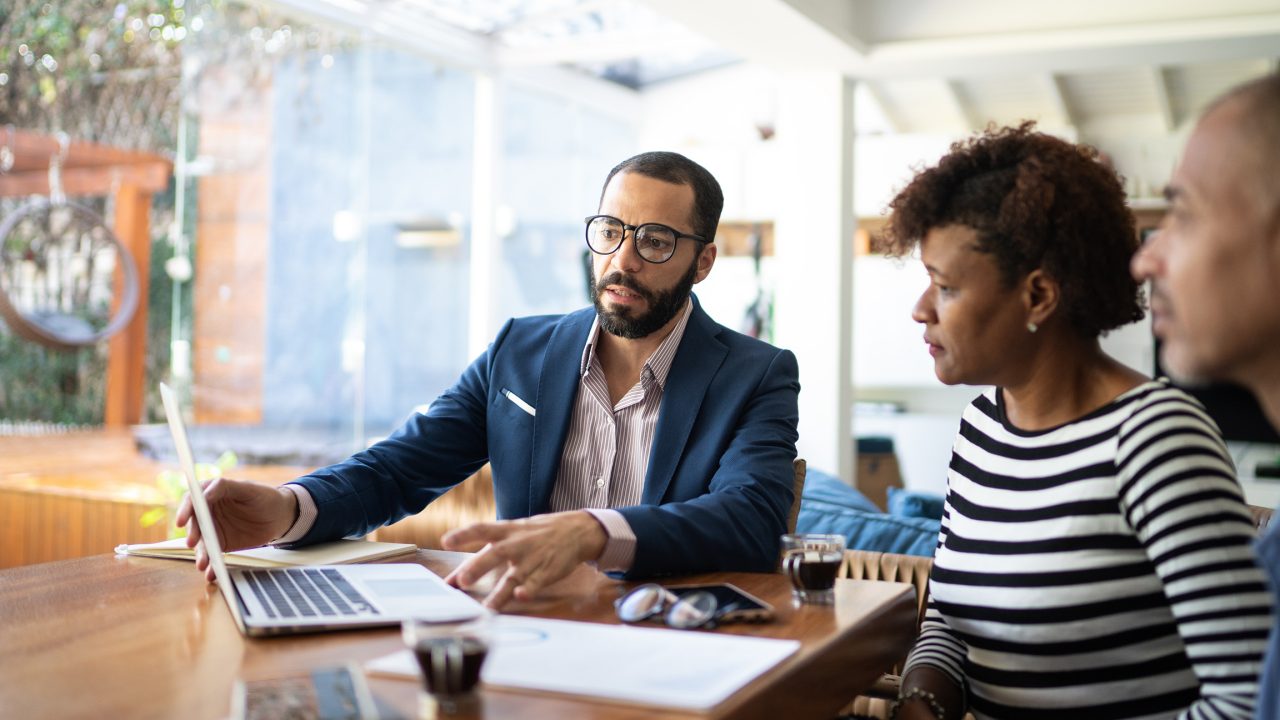 A man sat at a table sharing showing his laptop screen to a woman next to him