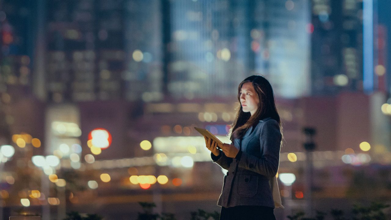A woman on her tablet device with a blurred shot of a city behind her