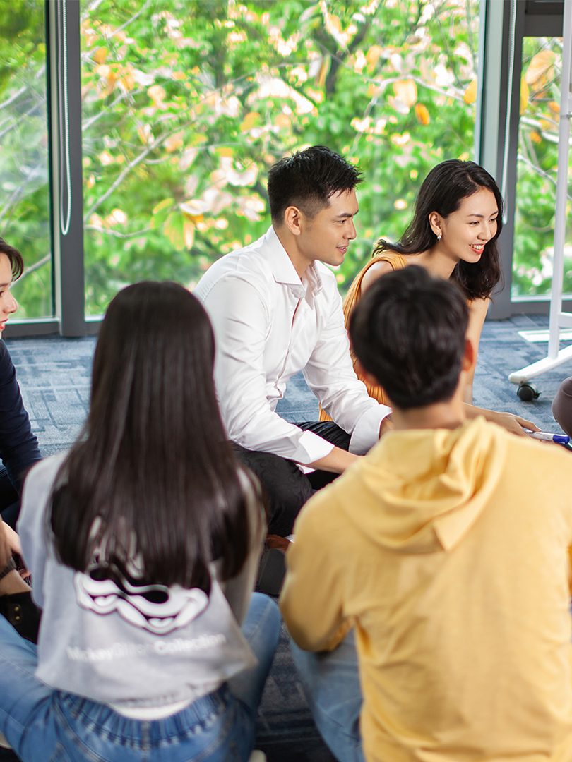 group of employees sitting on floor in front of a whiteboard, looking at a clipboard