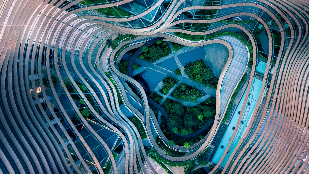 Aerial view of a modern architectural complex with flowing curved structures surrounding a lush central garden.
