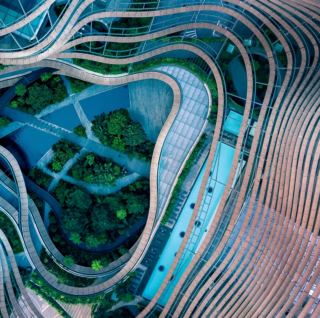 Aerial view of a modern architectural complex with flowing curved structures surrounding a lush central garden.