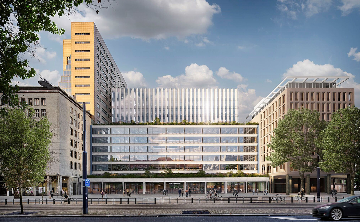 Modern office building with a glass facade and vertical white panels, surrounded by older buildings and trees. People are walking and cycling in front of the building on a city street under a partly cloudy sky.