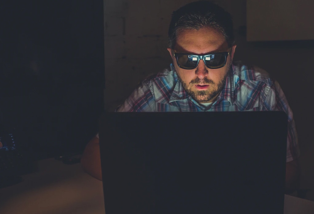 Man with sunglasses on laptop in dark room