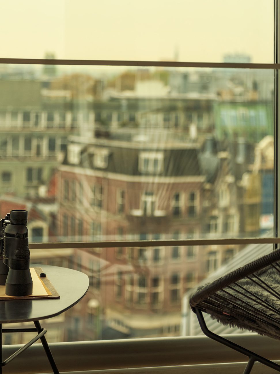 two chairs with table in between holding binoculars and notepad, facing out at buildings