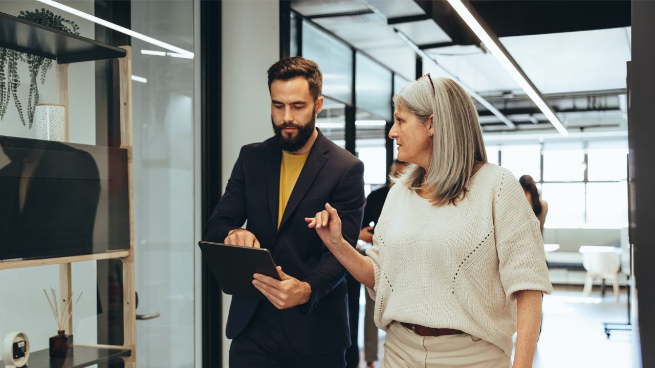 A man and woman in a work office talking in the corridor. 