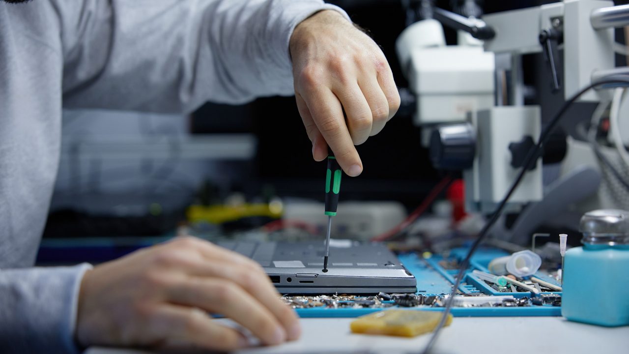 Person repairing a laptop with a screwdriver