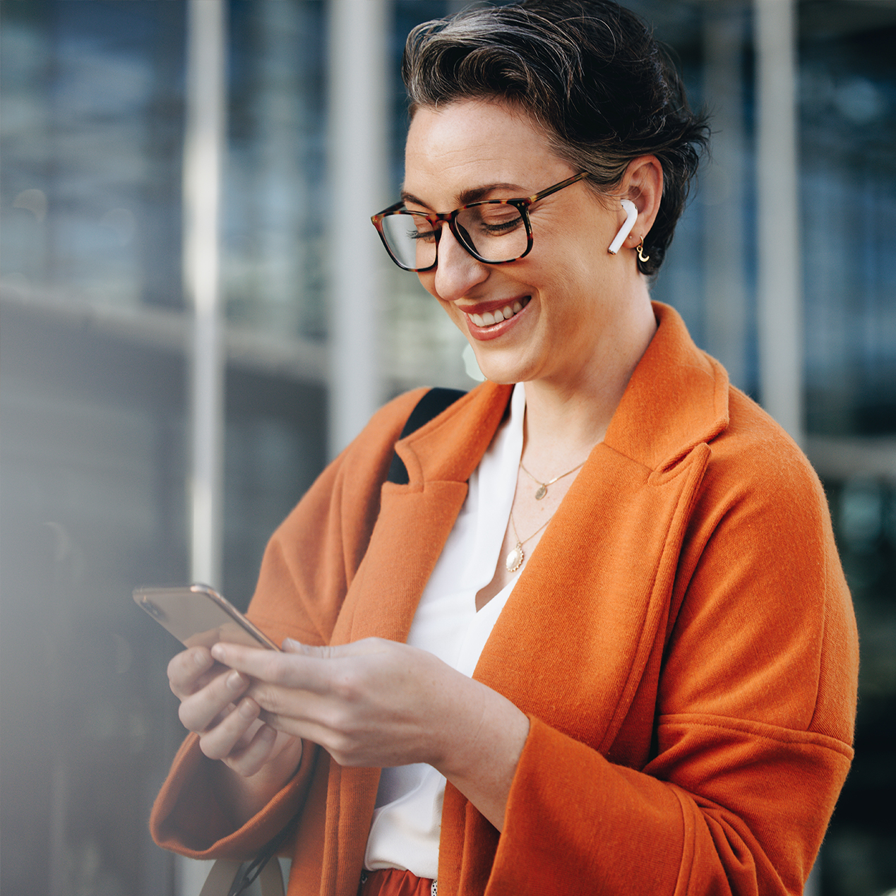 a close up image of a woman in an orange coat with her phone in her hand 