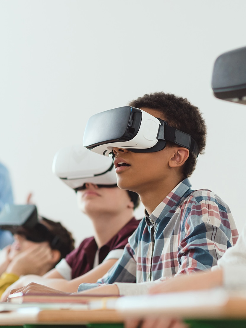 Multicultural school children using virtual reality headsets and teacher standing behind