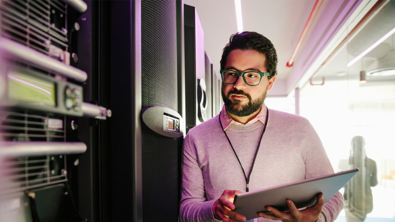 Focused male IT technician with digital tablet working in network server room