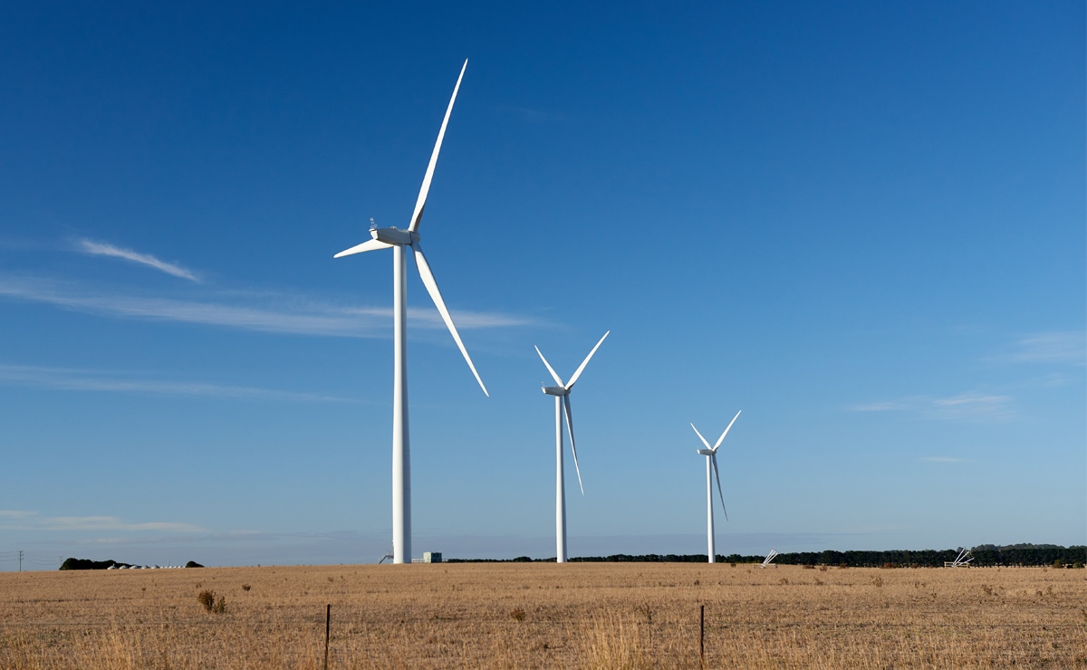 Three wind turbines standing in an open field under a clear blue sky, generating renewable energy.