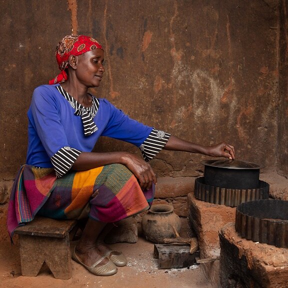 A woman of African descent cooking on an earthen stove