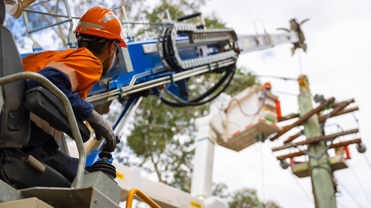 A utility worker operates machinery near a power pole during maintenance