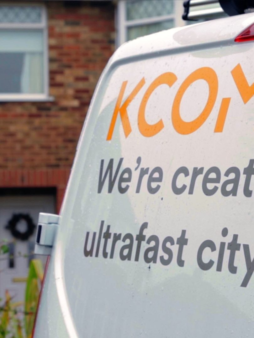 kcom van with worker in hi-vis climbing a ladder on wall of a home in background