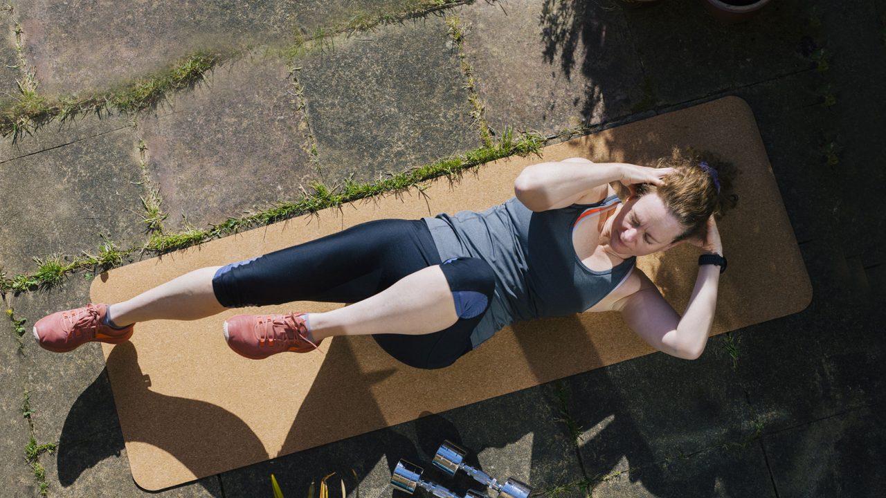 A woman on an beige workout mat doing exercise crunches