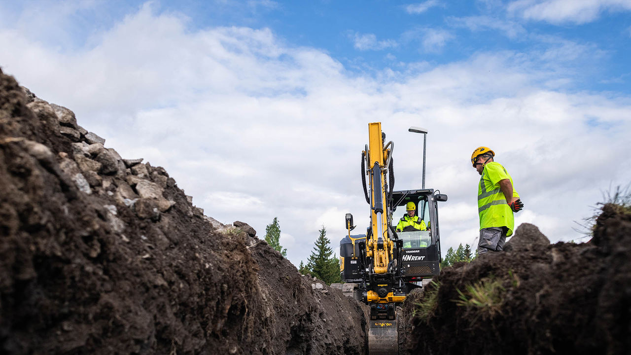 Workers installing a yellow utility pipe in a trench with heavy machinery