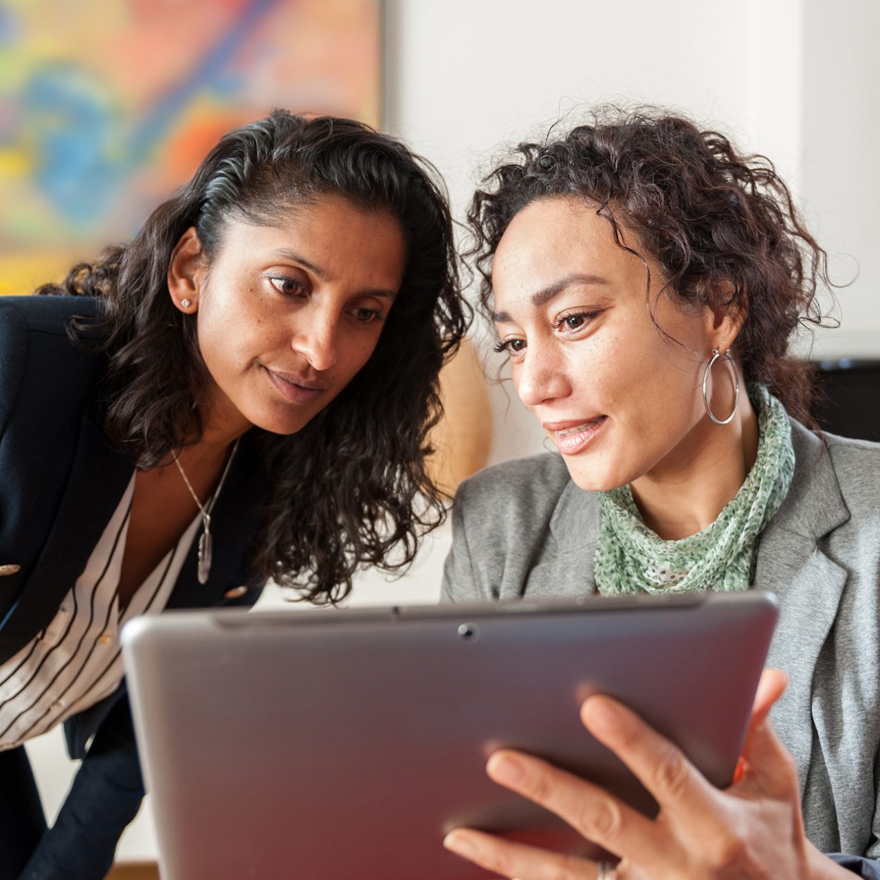 Two businesswomen looking at a tablet computer, discussing a topic